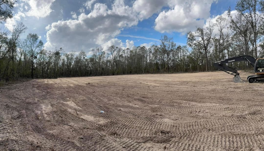 Cleared land with machinery in a forested area under a cloudy sky.