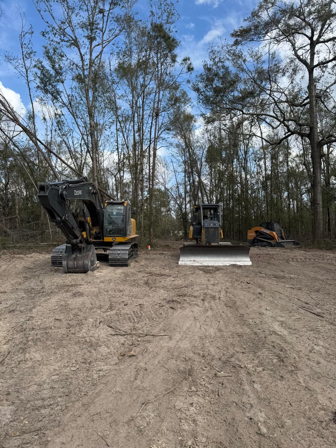 Excavators and bulldozers on a cleared land site surrounded by trees.