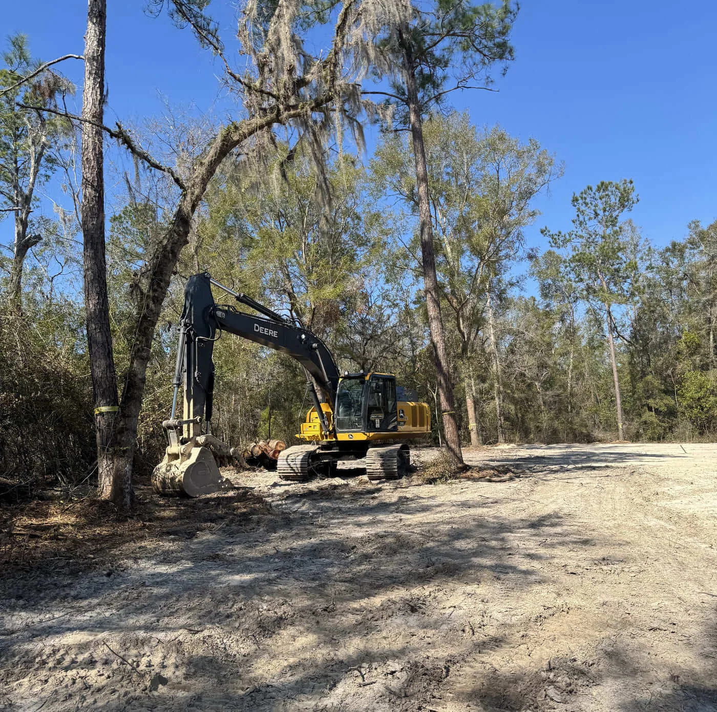 Deere excavator edge of cleared sand lot marked trees columbia county